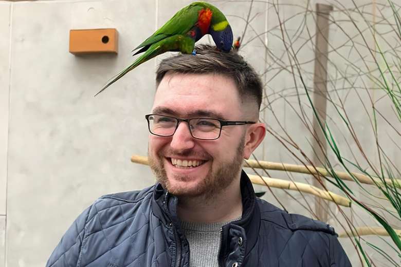 Barry Tickle smiling outdoors with a lorikeet parrot perched on his head